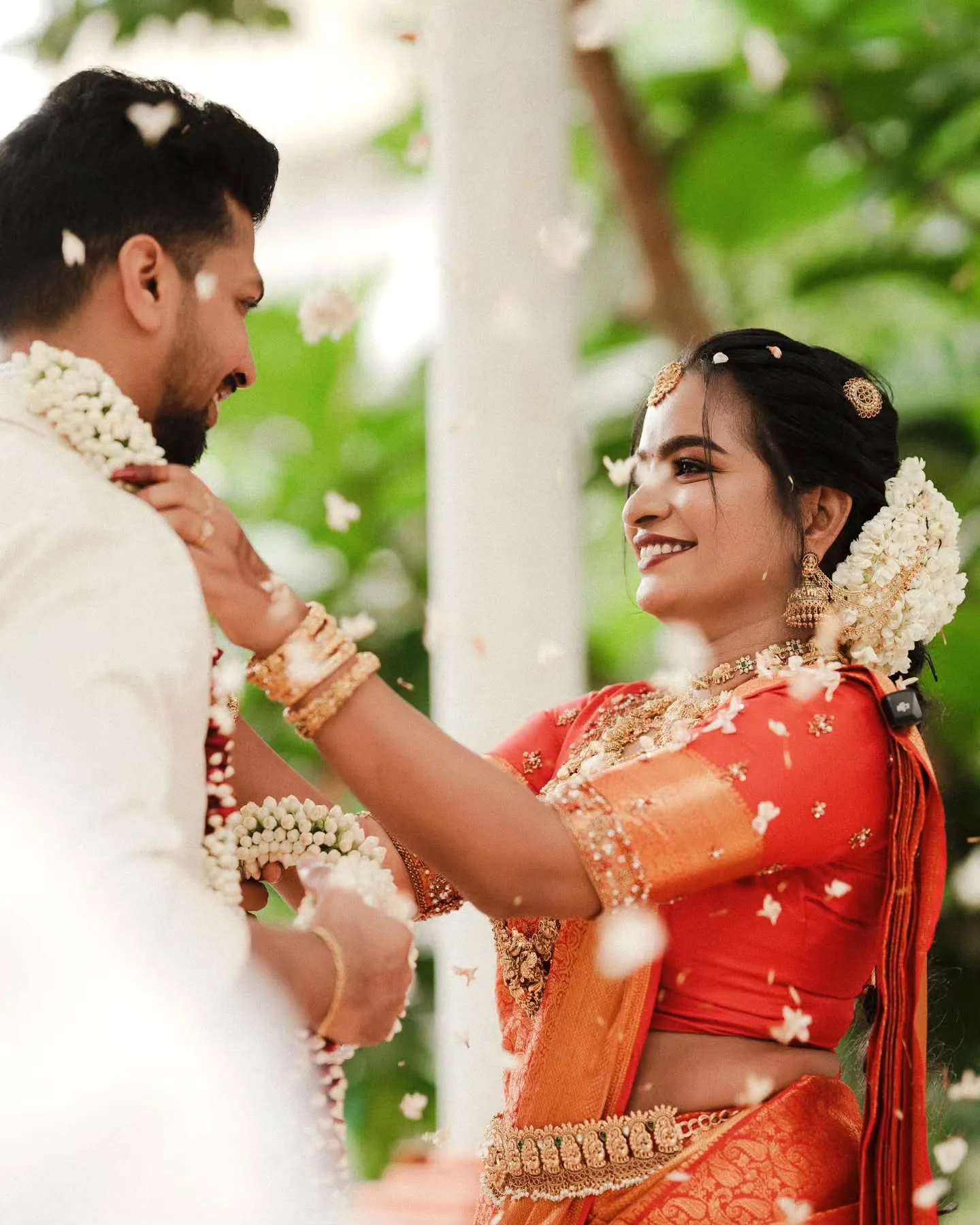 Petals fall as the groom places the wedding garland over the bride