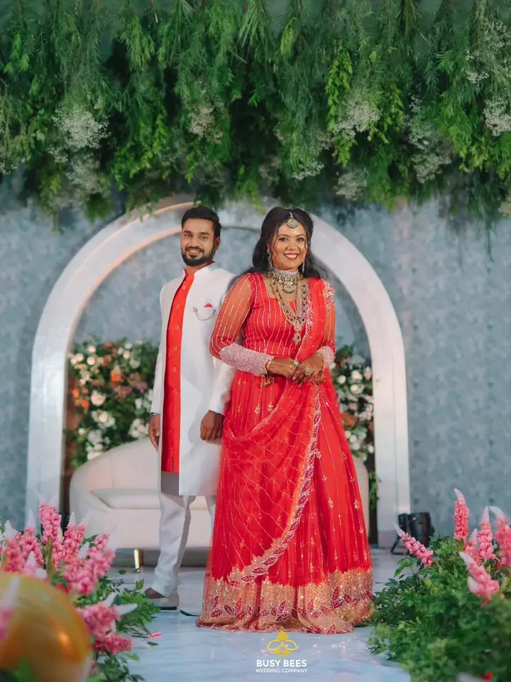 Bride in a red lehenga and groom on a floral engagement stage