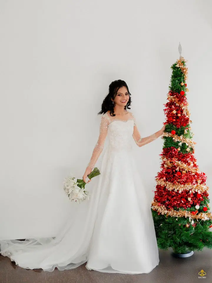 Bride in a white gown holding a bouquet beside a decorated Christmas tree