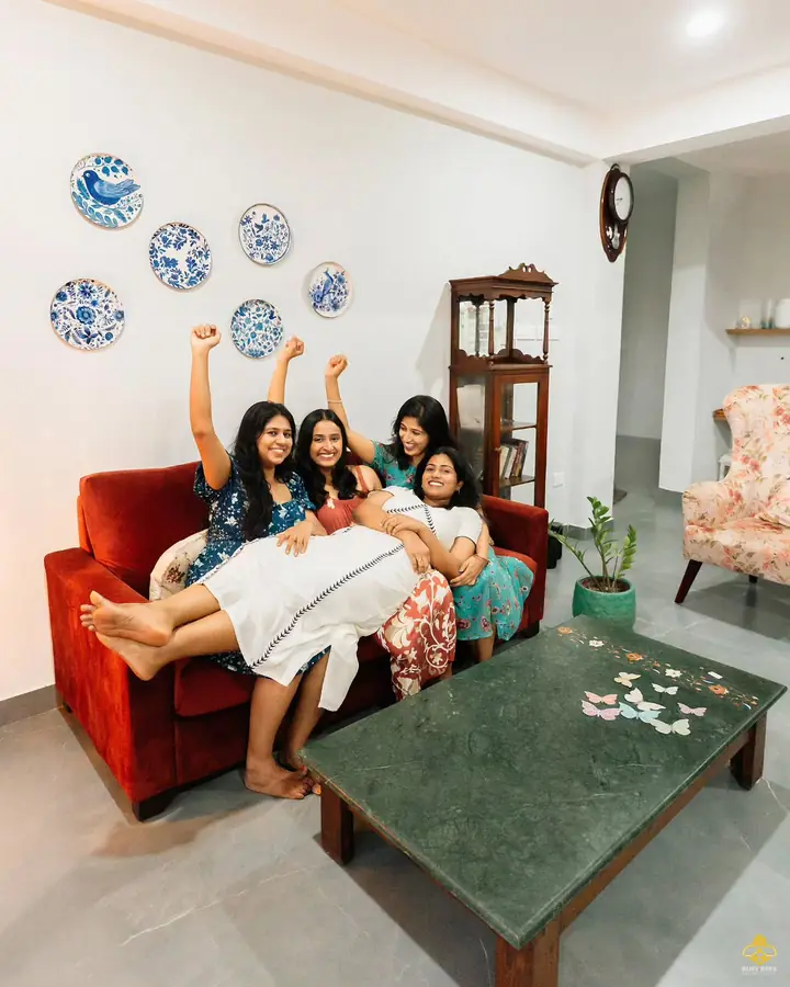 Bridesmaids pile onto a red sofa around the bride, mid-celebration
