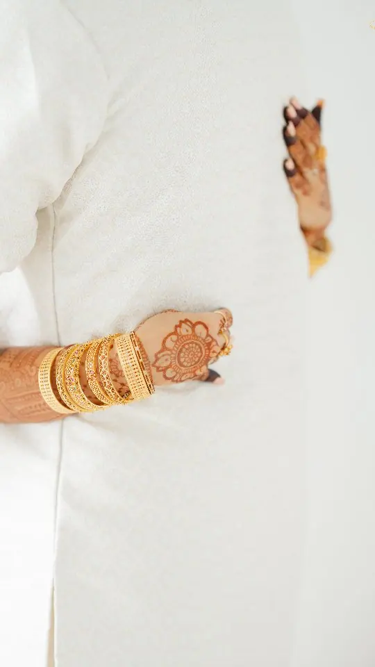 Close-up of henna hands and gold bangles resting against a white mundu