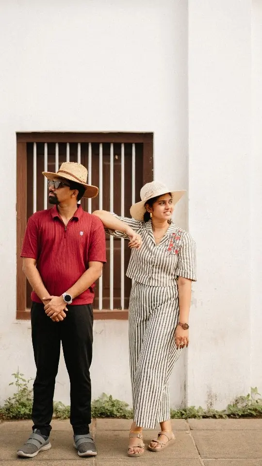 Couple in sun hats leaning against a whitewashed wall in a casual portrait