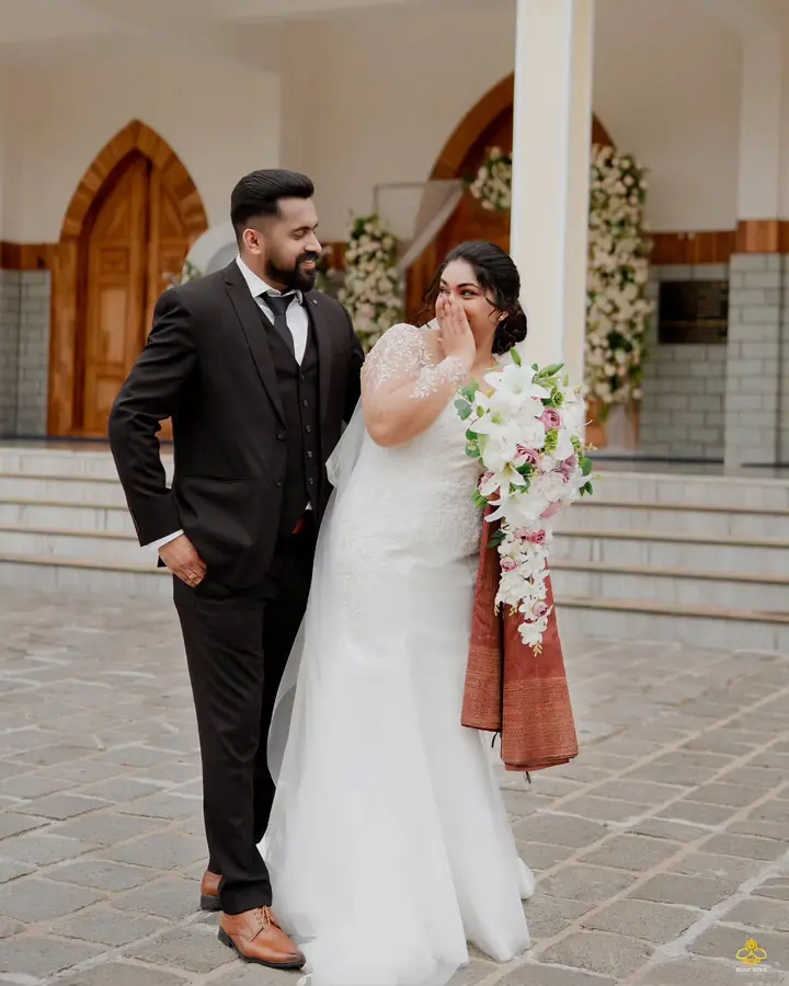 Bride laughs beside the groom outside the church, bouquet in hand