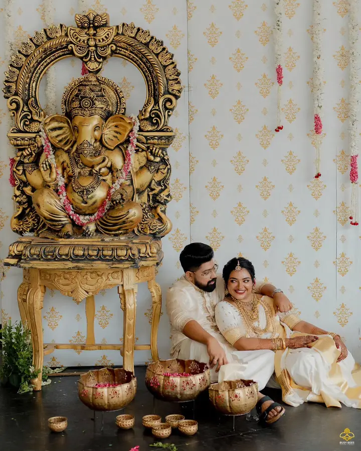 Couple seated beside a gilded Ganesha idol with oil lamps and flowers