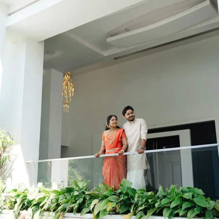 Wide frame of the couple on a white balcony above a screen of green leaves