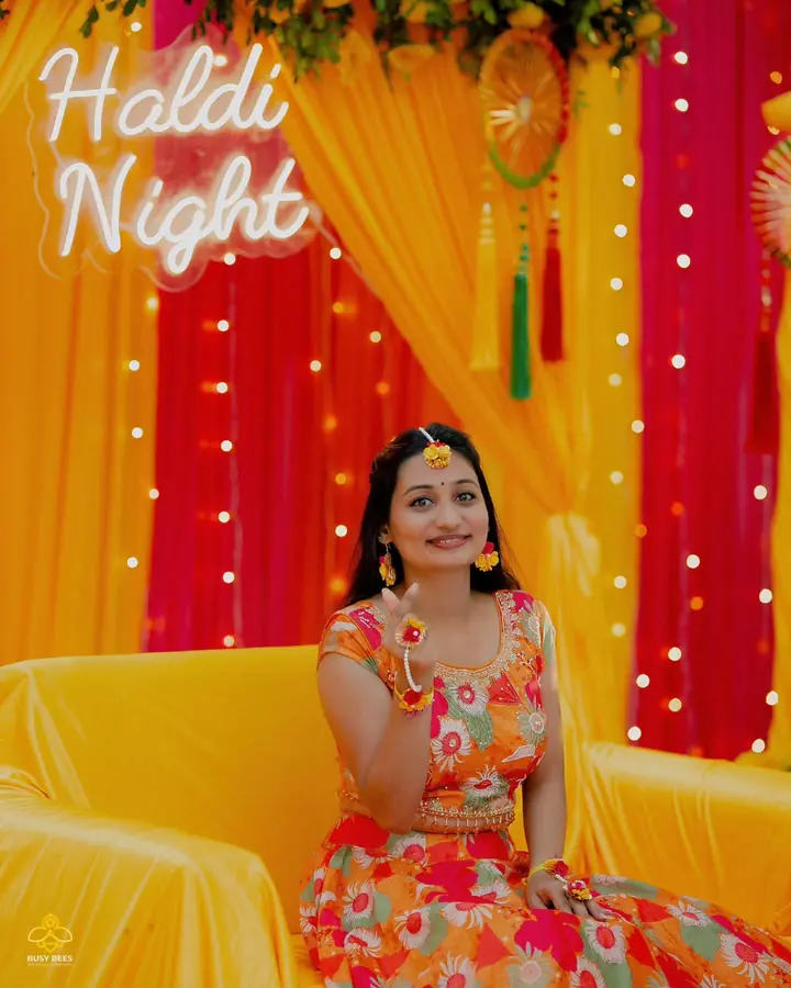 Bride on a yellow settee against pink drapes at her haldi night