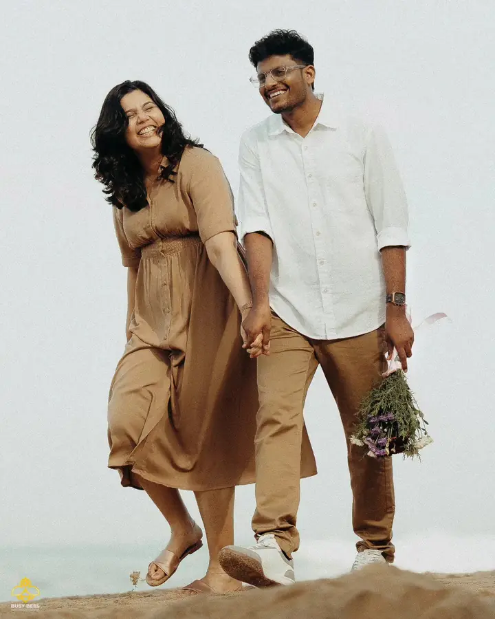 Couple walk barefoot along the shoreline holding a bunch of wildflowers