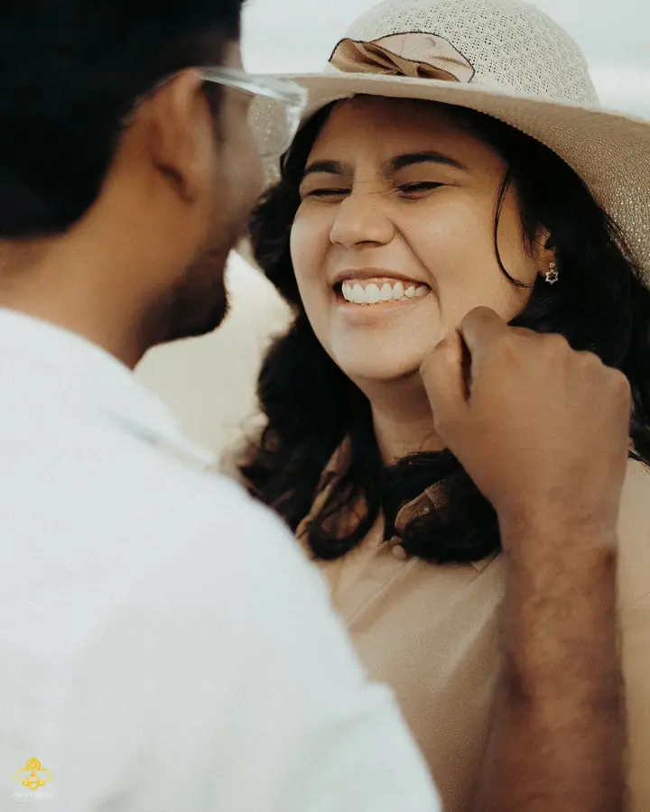 The bride laughs in a wide straw hat, close in against the groom