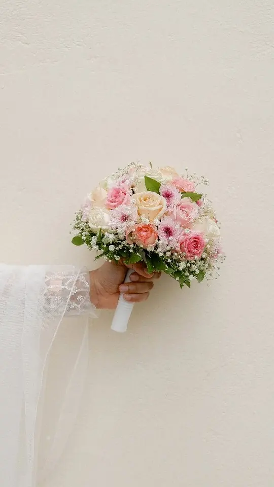 Bouquet of pink and cream roses held against the bride's white gown
