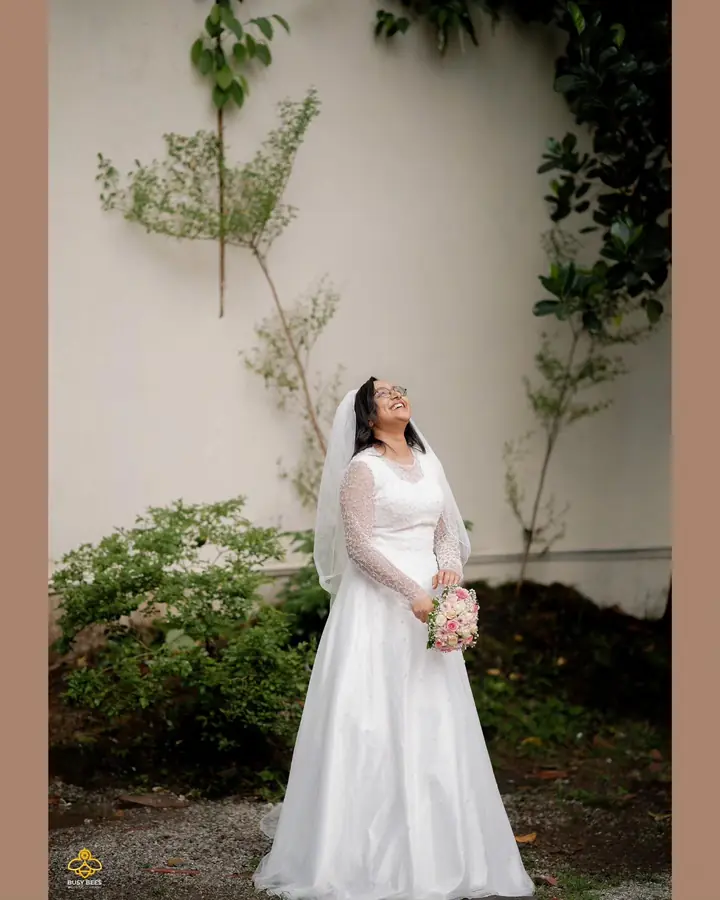 Bride in a white gown and veil beside a whitewashed garden wall